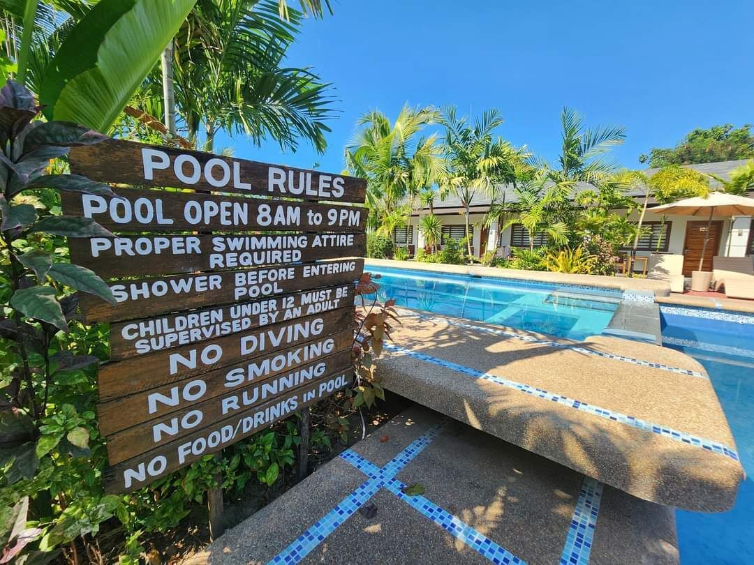 Un letrero de madera con las normas de la piscina, incluyendo horarios y requisitos.