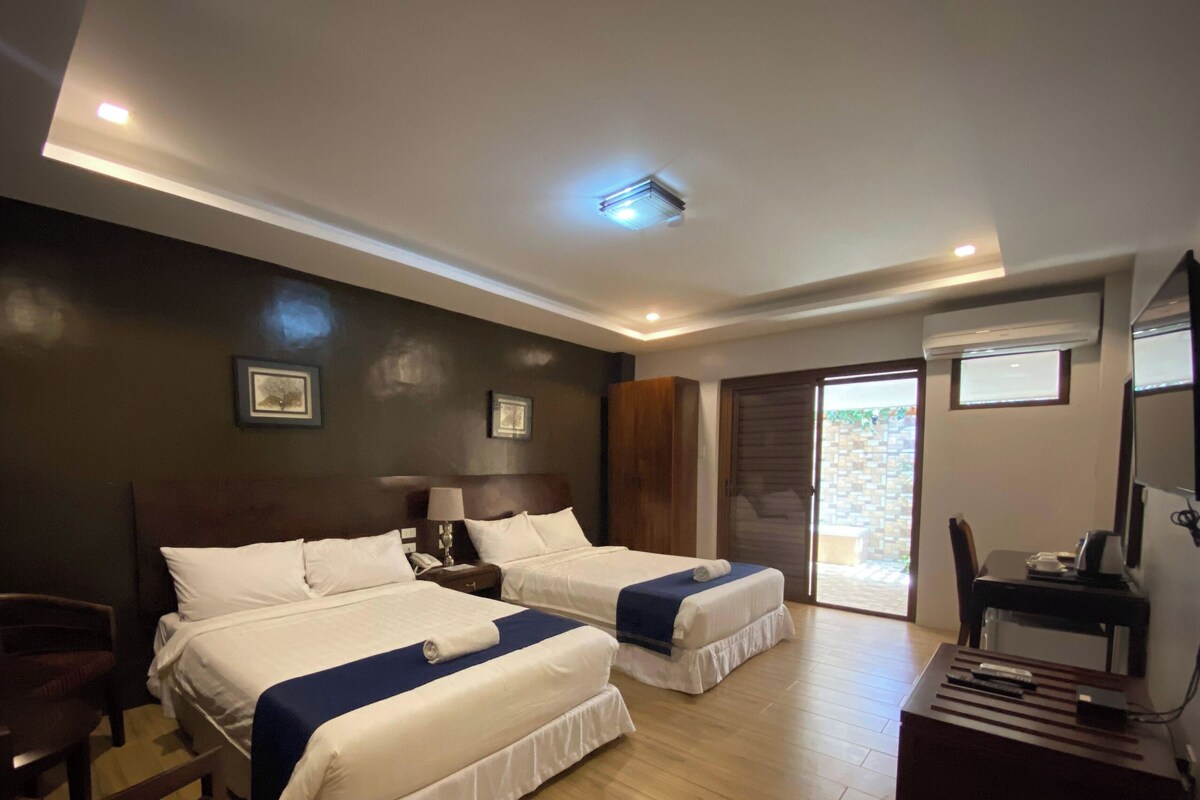 A hotel room with two beds, a desk, a chair, and a large window.