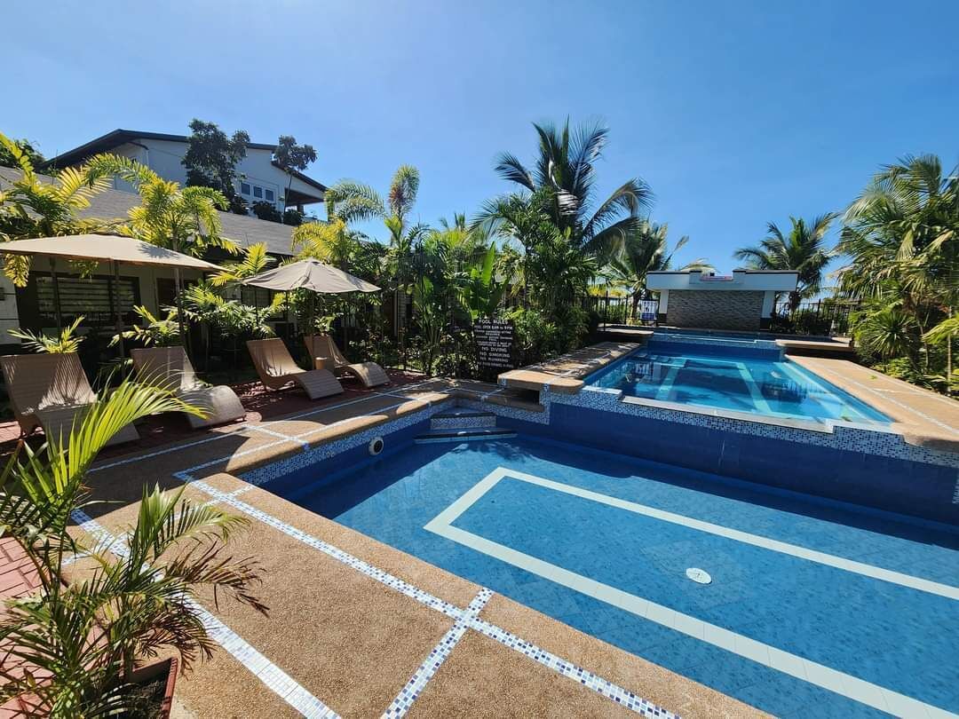 A swimming pool with lounge chairs and umbrellas, surrounded by palm trees and a building.