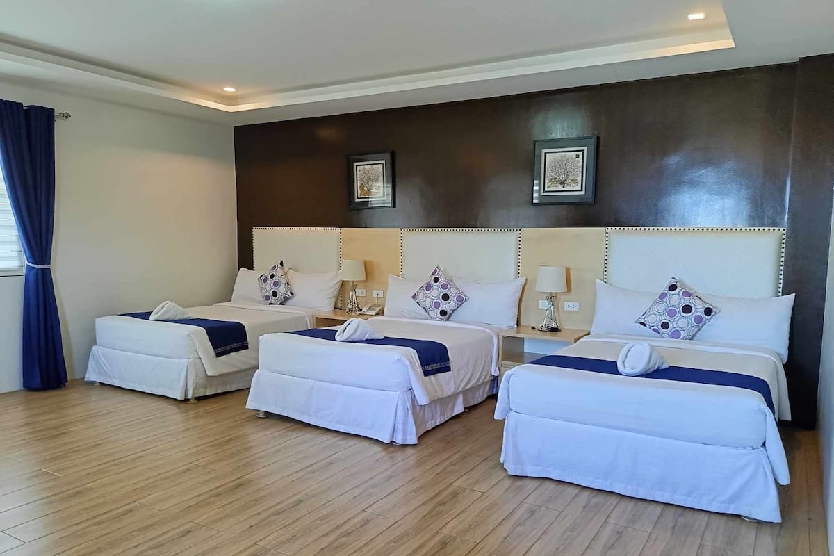 A hotel room with three beds, wooden flooring, and a dark wall with framed artwork.