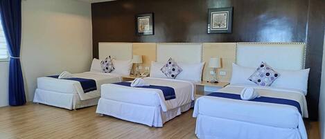 A hotel room with three beds, wooden flooring, and a dark wall with framed artwork.