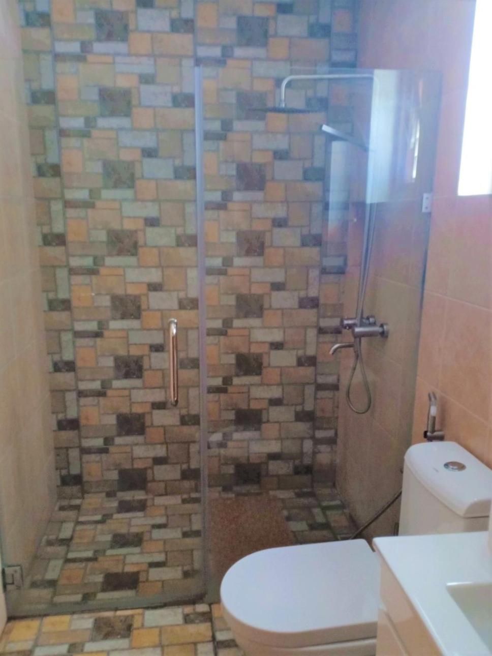 A bathroom with a shower enclosure, a toilet, and a sink.