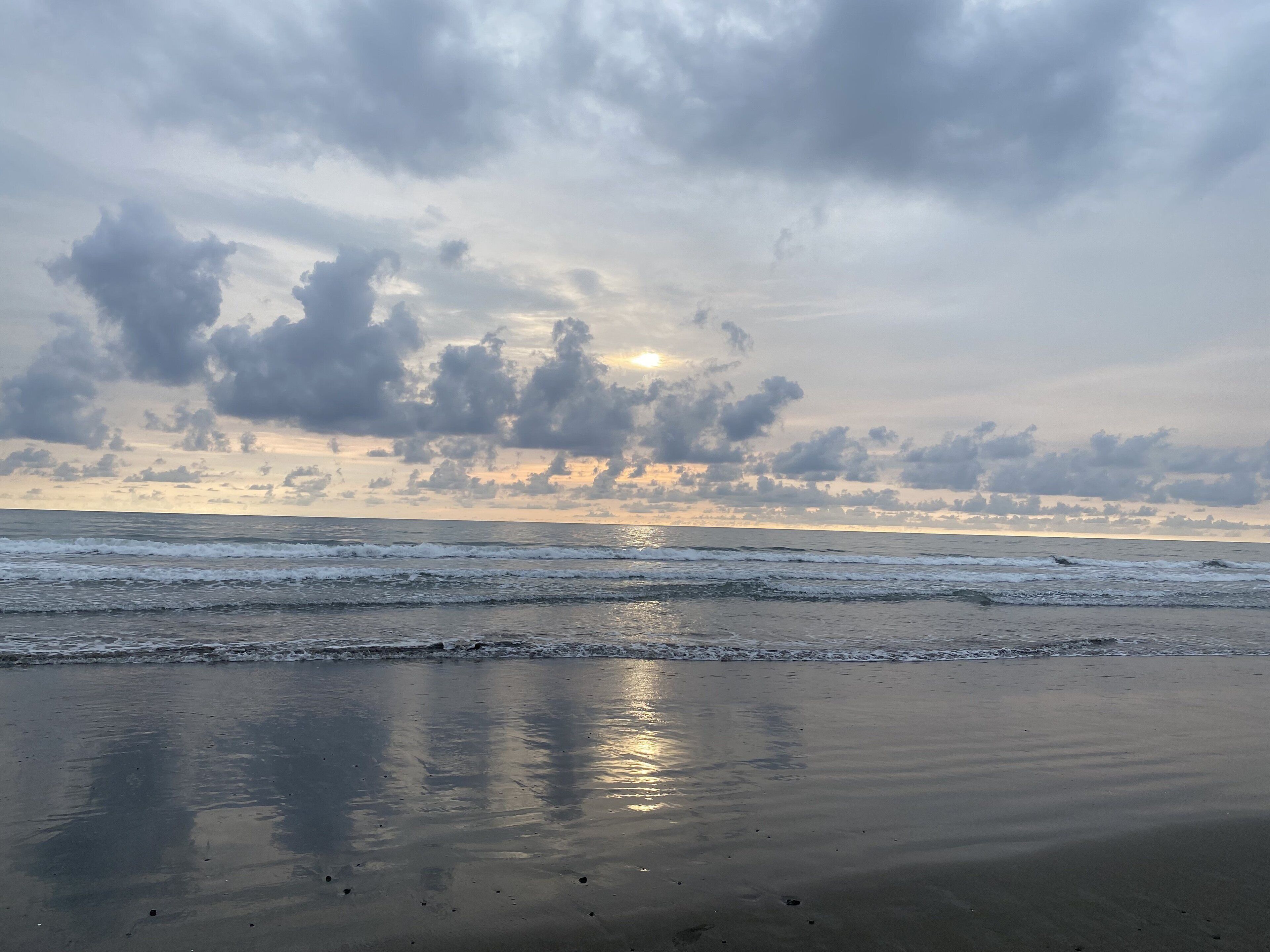 A beach with calm waves and a cloudy sky.