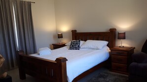 Un lit bien fait, avec du linge de lit blanc, deux tables de chevet avec des lampes, une tête de lit en bois, un tapis foncé et une chaise.