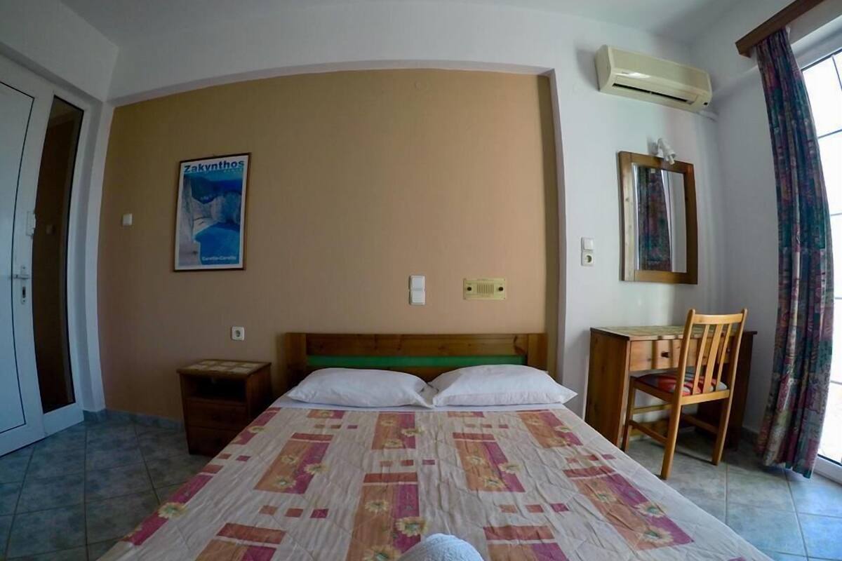 Ein Hotelzimmer mit Bett, Schreibtisch, Stuhl, einem Poster an der Wand und einer Klimaanlage.