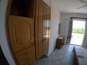 Ein Zimmer mit großem Holzschrank, kleinem Holztisch und einer Schiebeglastür, die zu einem Außenbereich führt.