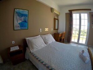 Ein Hotelzimmer mit Bett, Schreibtisch, Stuhl, einem Fenster mit Vorhängen und einem Poster an der Wand.