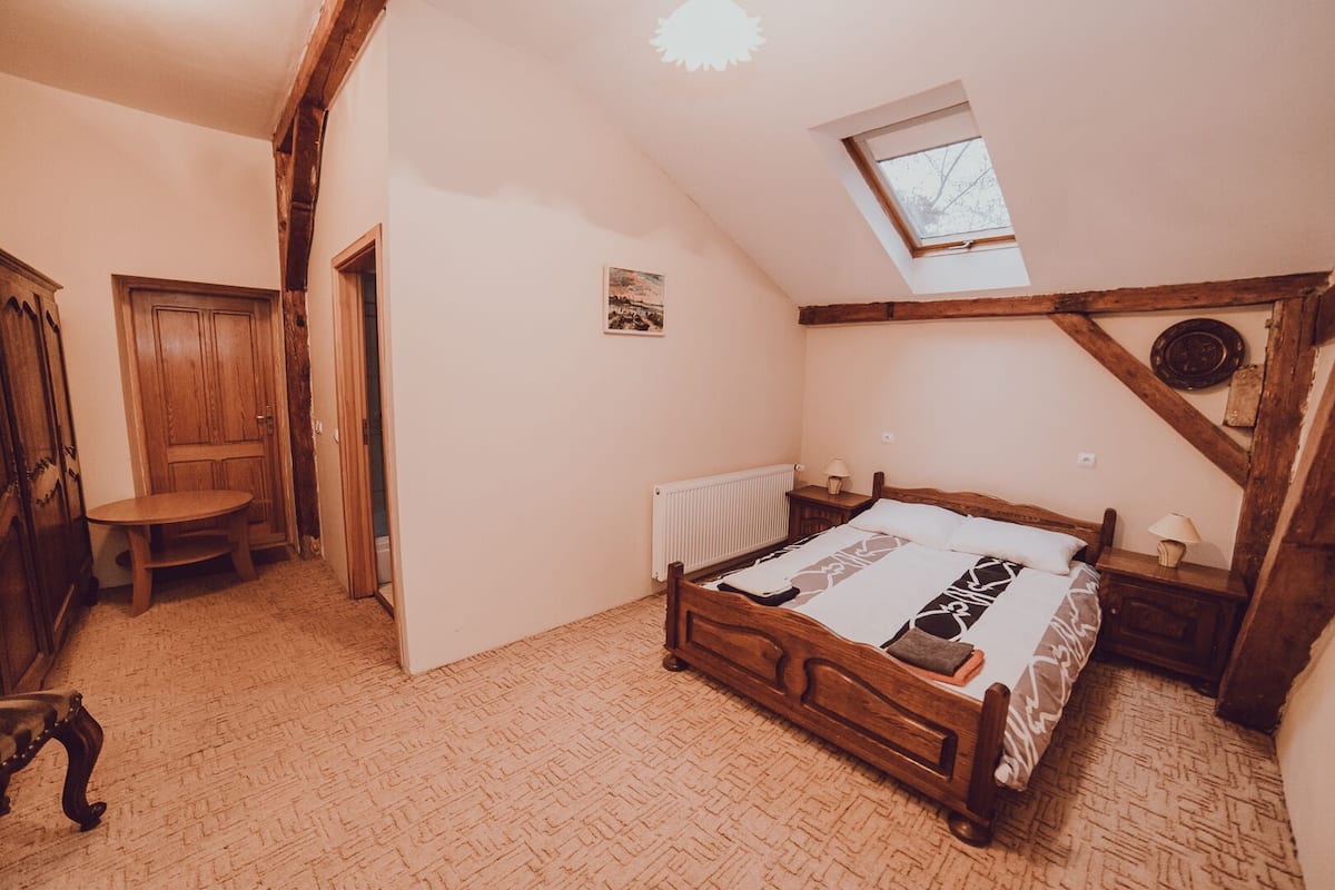 A bedroom with a wooden bed, a small table, a radiator, and a sloped ceiling with a skylight.