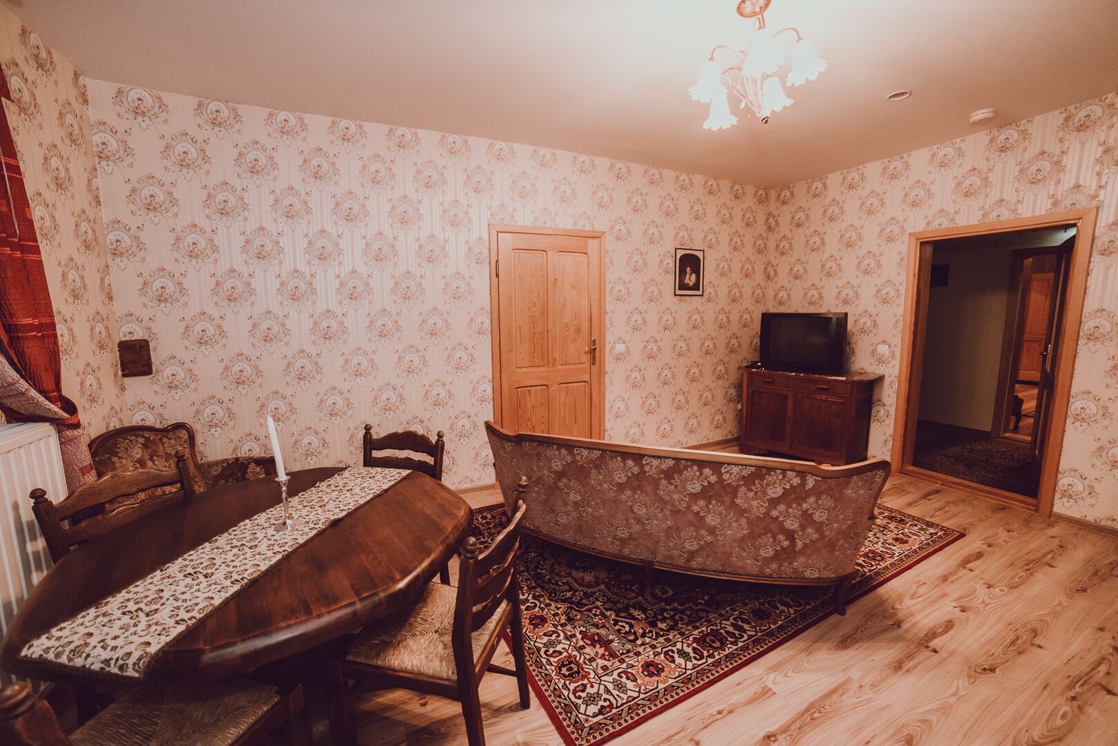 Ruokailuhuone, jossa on puinen pöytä, tuoleja, kuviollinen matto, televisiotauluko, ja ovi.