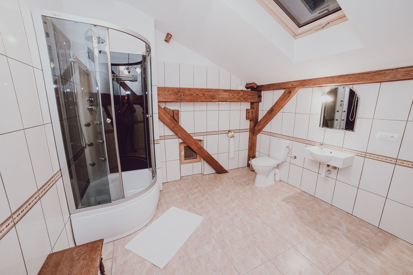 A bathroom with a glass-enclosed shower, a wooden beam ceiling, a toilet, and a sink.