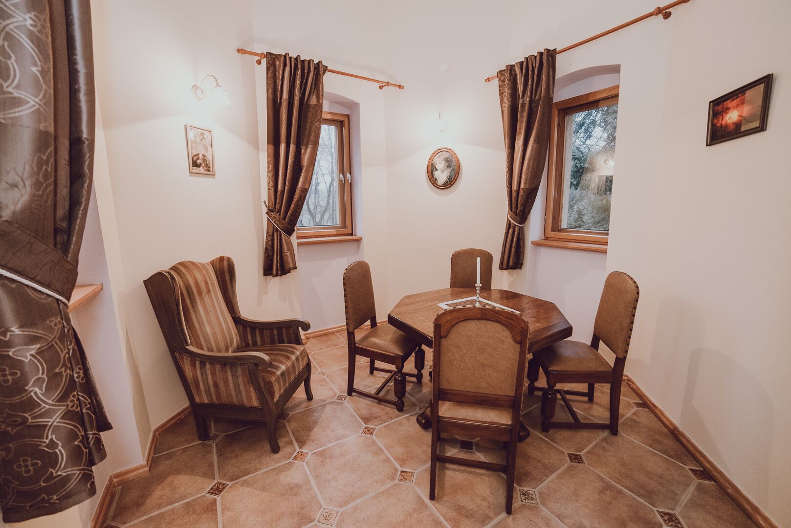 Ein Essbereich mit einem runden Tisch, sechs Stühlen, Holzboden und zwei mit Vorhängen drapierten Fenstern.