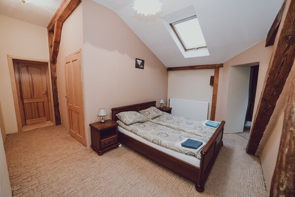 A bedroom with a sloped ceiling, a skylight, a wooden bed, a nightstand, and a radiator. - Pałac Kursko (Miedzyrzecz)