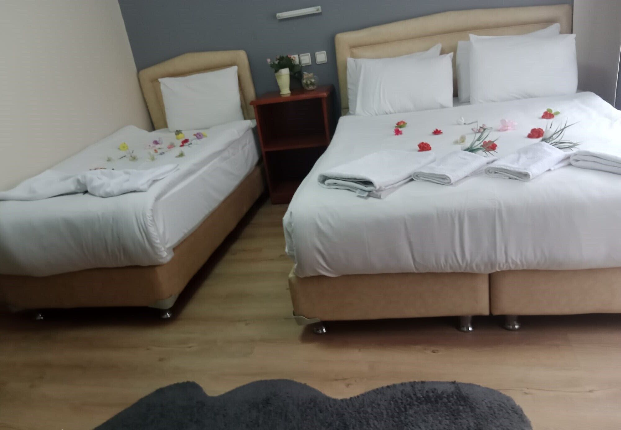 Ein Hotelzimmer mit zwei Einzelbetten und einem Doppelbett, jeweils mit weißer Bettwäsche und floralen Verzierungen.
