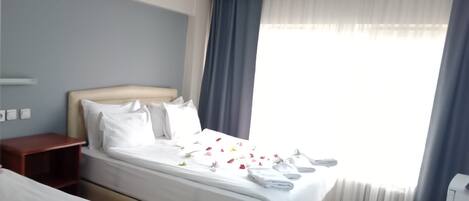 Habitación de hotel con una cama grande, una mesita de noche y un ventanal con cortinas.