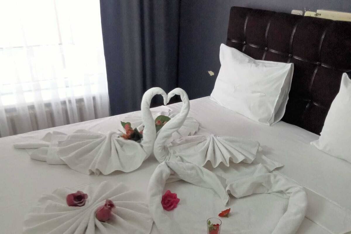 A hotel room with a neatly made bed featuring swan-shaped bedspreads and rose decorations.