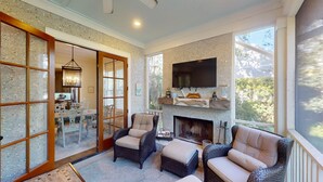 A cozy living room with wicker furniture, a fireplace, and a TV mounted above it.