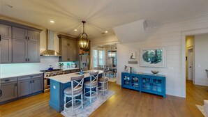 A spacious kitchen with a central island, grey cabinets, and a blue bar area.