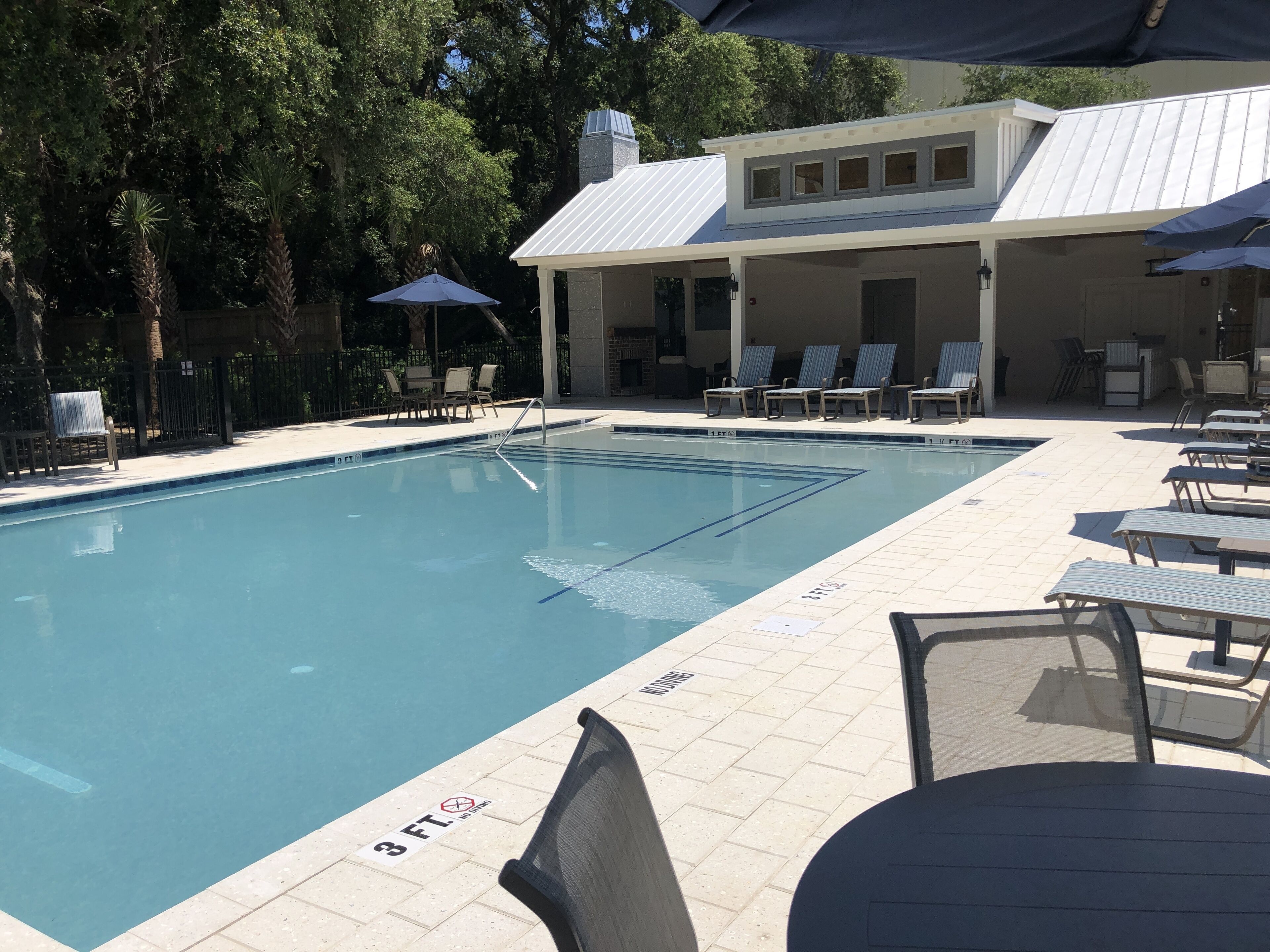 A swimming pool with lounge chairs and umbrellas, surrounded by trees.