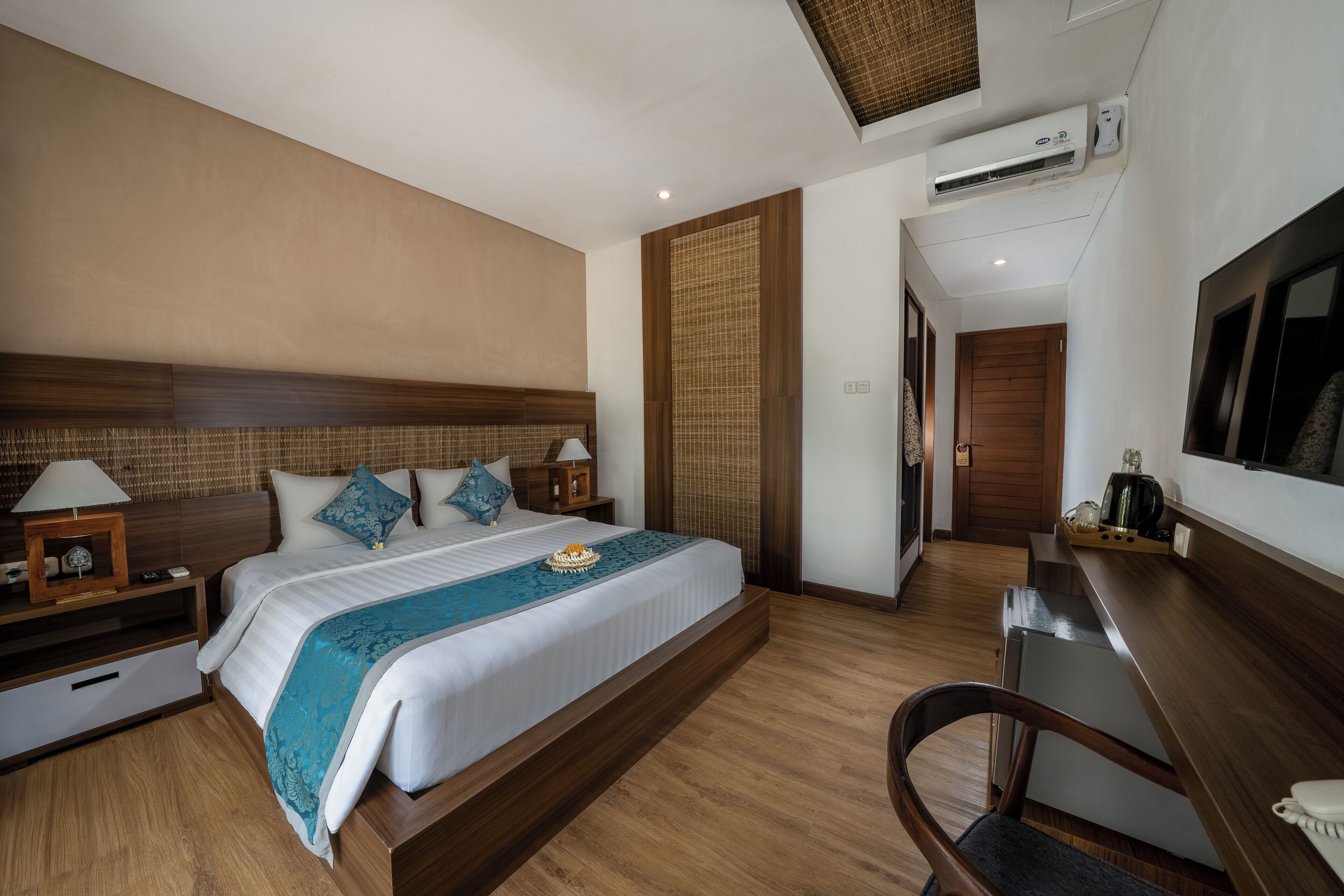 A modern hotel room with a wooden bed, bedside tables, a desk, and an air conditioning unit.