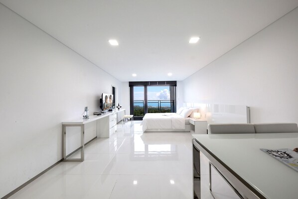 A modern hotel room with a large bed, a desk, a TV, and a view of the sea.