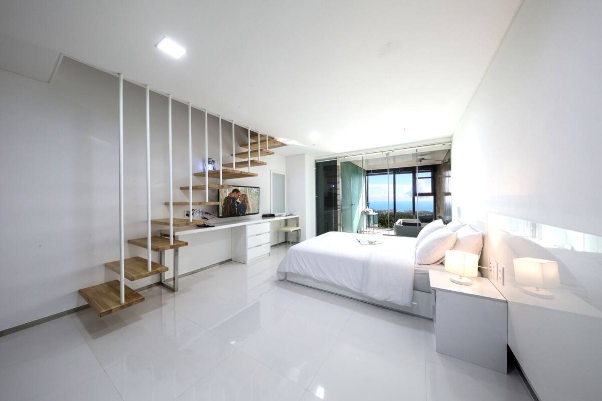 A modern bedroom with a large bed, a desk, and a staircase.