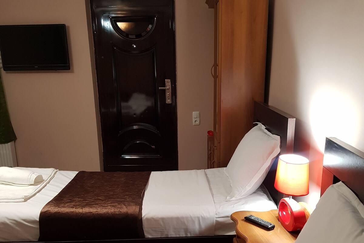 A hotel room with two beds, a door, a TV, a lamp, and a remote control.