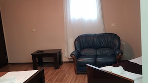 Una habitación con piso de madera, un sofá de cuero, una mesita y una cama con sábana blanca.