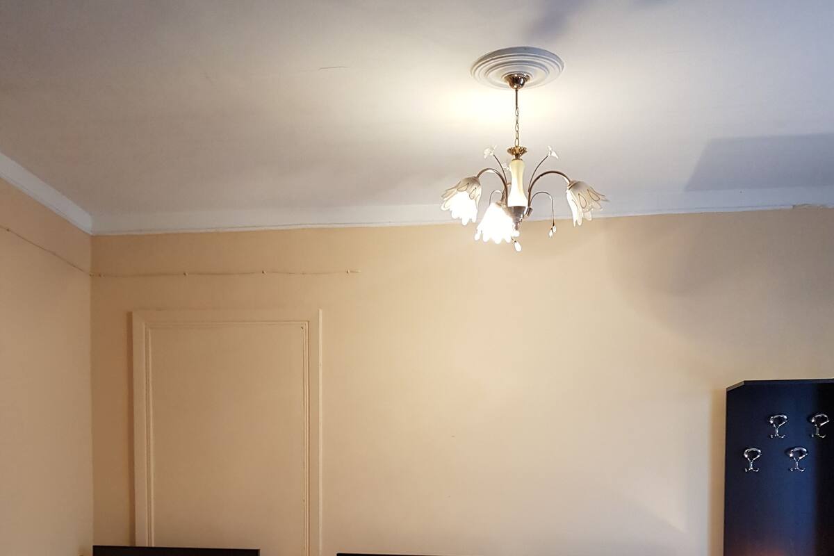 A hotel room with two single beds, a chandelier, a nightstand with a lamp, and a wardrobe.