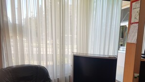 Una habitación con un sillón de cuero, un mueble negro y un ventanal con cortinas traslúcidas.