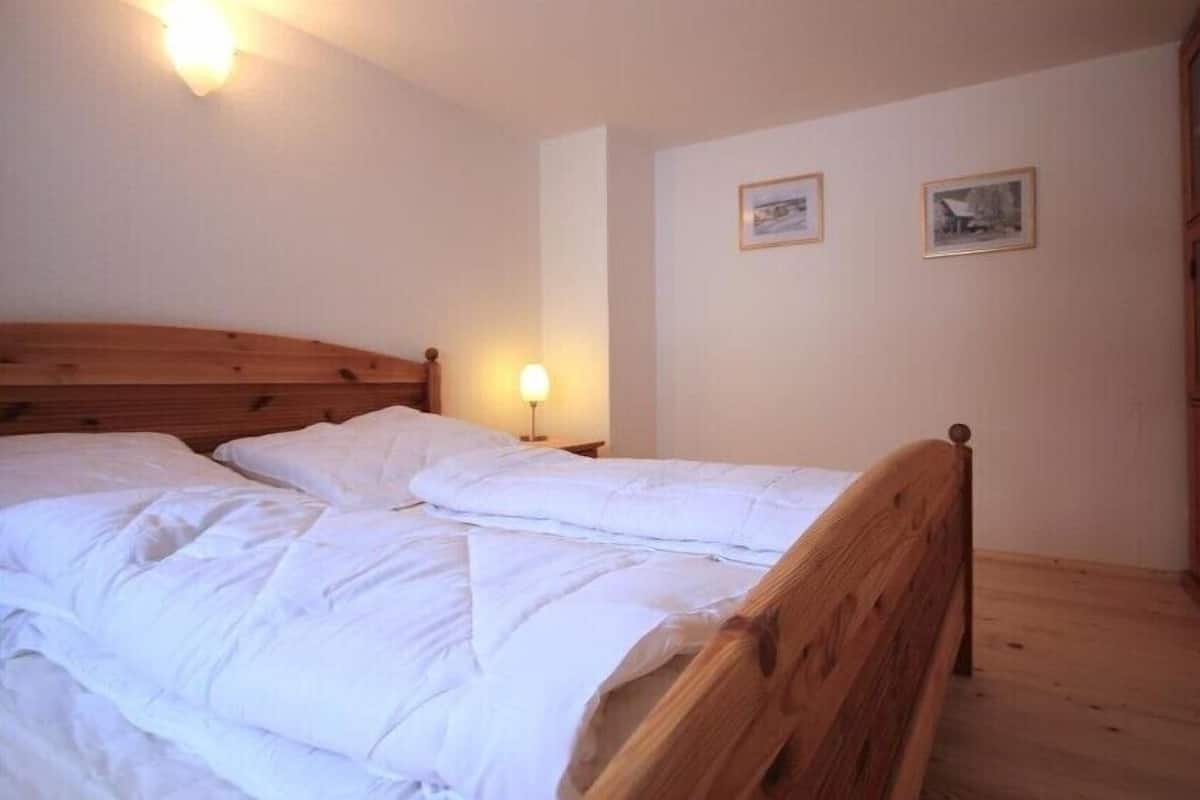 Un dormitorio con una cama de madera, una mesita de noche con lámpara y dos cuadros enmarcados en la pared.