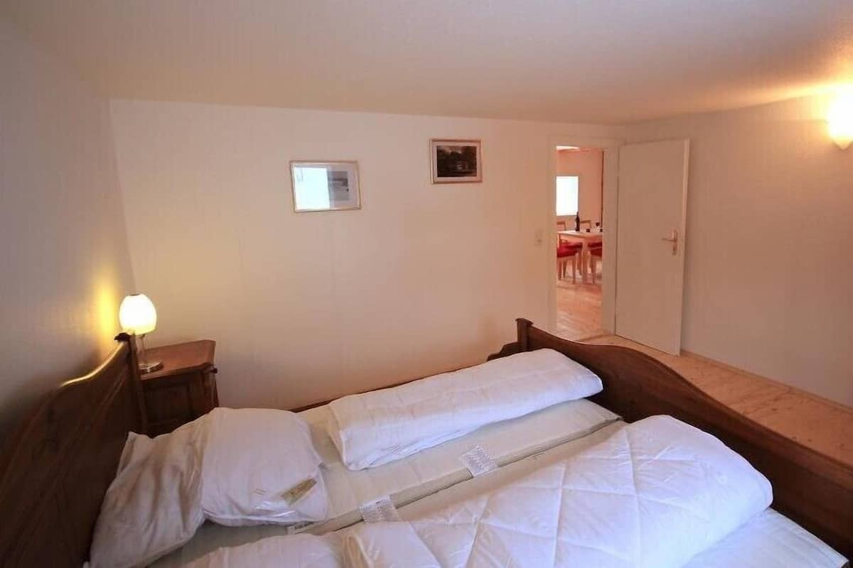 Una habitación de hotel con una cama, una mesita de noche, una lámpara y una puerta que da a un comedor.