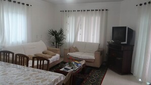 Een woonkamer met een bank, een eettafel, een televisie en een plant.