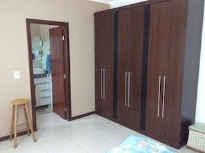 A bedroom with a wardrobe, a stool, and a bed.