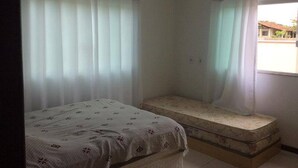 Een kleine, zwak verlichte kamer met een enkel bed en een matras op de vloer.