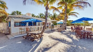 En restaurang vid stranden med uteservering, palmer och en sandstrand.