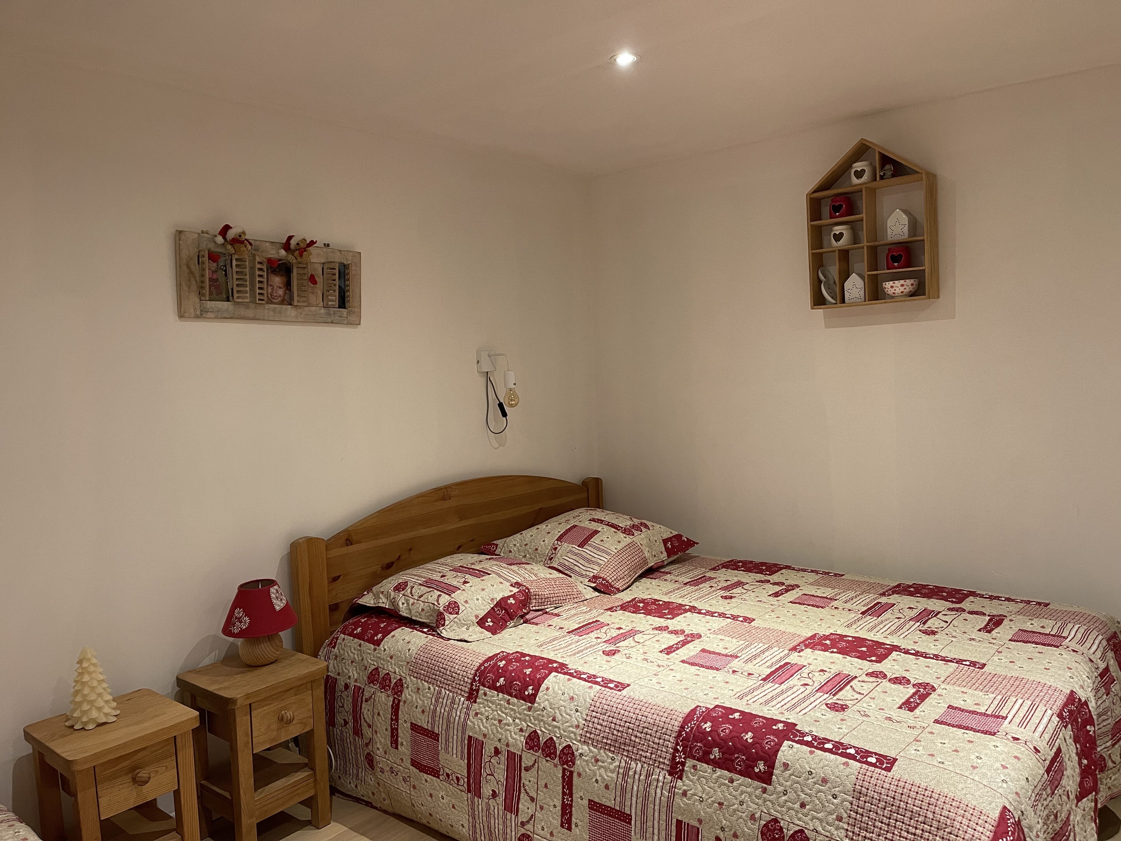 Une chambre à coucher avec un lit en bois, une table de chevet avec une lampe, une étagère murale ornée d’objets décoratifs et une horloge murale.