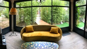 A room with a yellow sofa, a patterned coffee table, and a view of a garden through large windows. - Independent cottage Val D'amour (Nages-et-Solorgues)