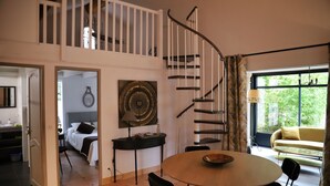 A modern interior with a spiral staircase, a dining area, a sofa, and a large window with a view of greenery. - Independent cottage Val D'amour (Nages-et-Solorgues)