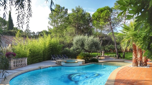 A swimming pool with a hot tub, surrounded by lush greenery and a tiled deck. - Independent cottage Val D'amour (Nages-et-Solorgues)