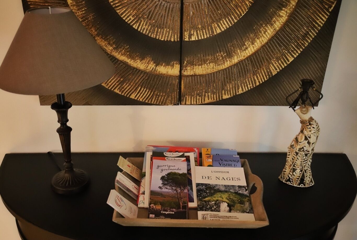 Une table avec une lampe, un objet décoratif et un plateau de livres.