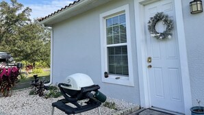 A house with a white exterior, a front door with a wreath, a window with blinds, and a grill in the driveway. - Private studio; big outdoor space  (Orlando)
