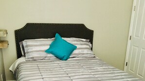 A bed with a striped bedspread and a teal pillow, a wooden headboard, and a white door in the background. - Private studio; big outdoor space  (Orlando)