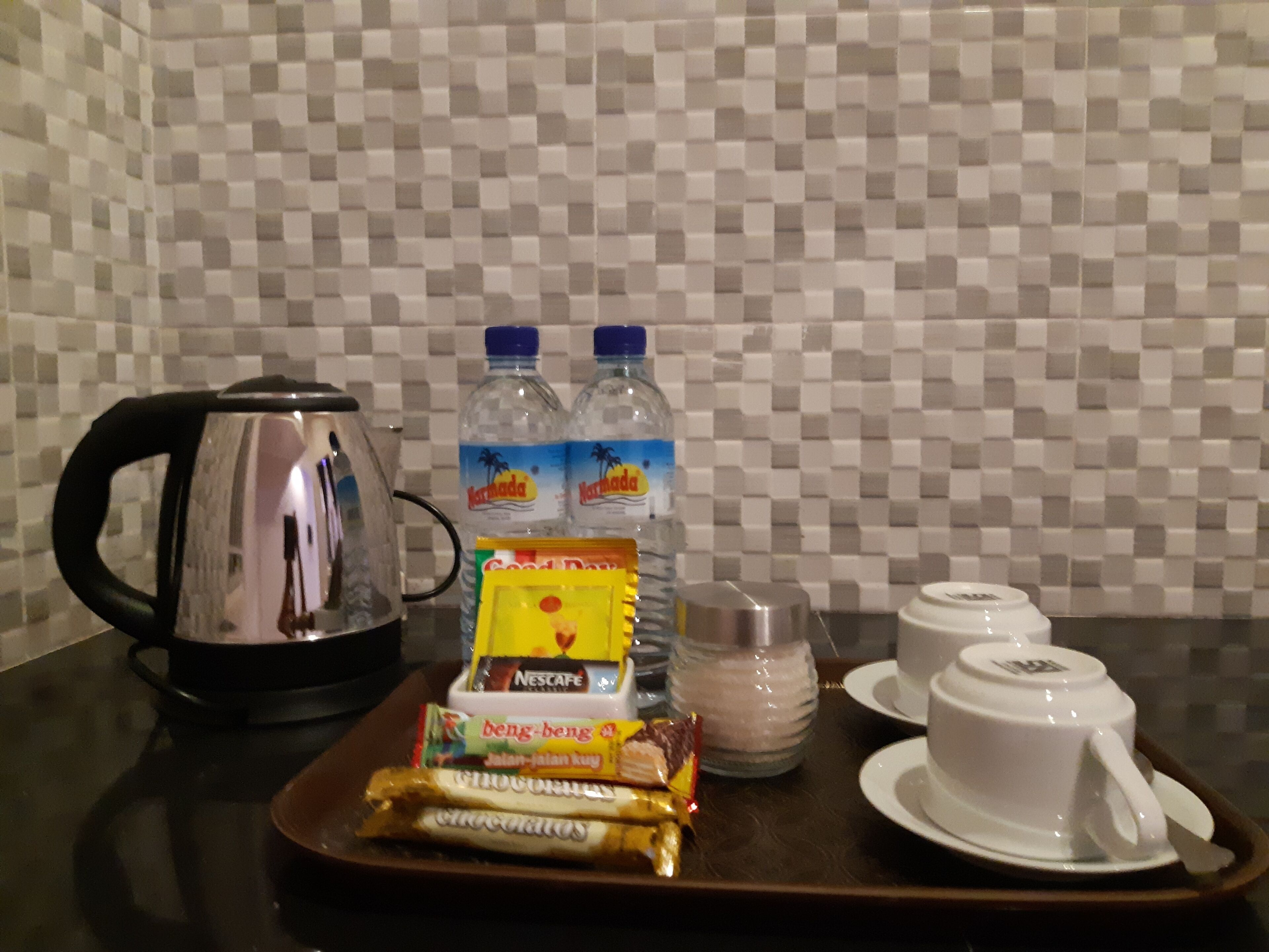 A tray with a kettle, bottled water, a Nescafe coffee pack, and packaged snacks.
