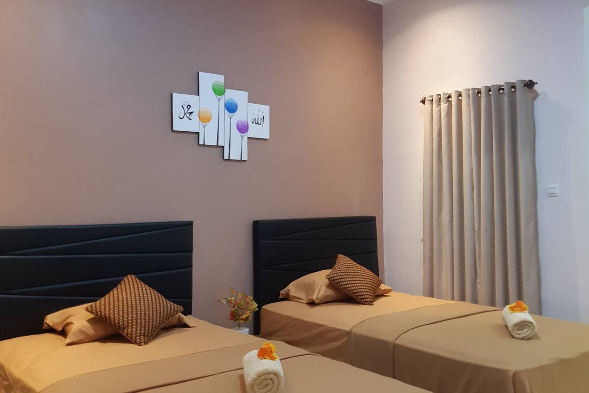 Habitación de hotel con dos camas, ropa de cama color beige, una lámpara en el techo, una obra de arte en la pared y una ventana con cortinas.