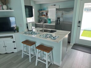 A modern kitchen with a central island, bar stools, a refrigerator, and a television.