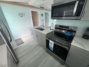 A modern kitchen with stainless steel appliances, a microwave, and a kettle on the countertop. - Bay Breeze - Cozy Beach Cottage across from the beach. Pet friendly! (Madeira Beach)