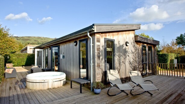 A modern spa building with a hot tub, lounge chairs, and a wooden deck. - Diamond Lodge - Hot Tub - Free WiFi & Parking - Pets Welcome (Cheddar)