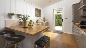 A modern kitchen with a central island, bar stools, a built-in oven, and a view to the outside. - Diamond Lodge - Hot Tub - Free WiFi & Parking - Pets Welcome (Cheddar)