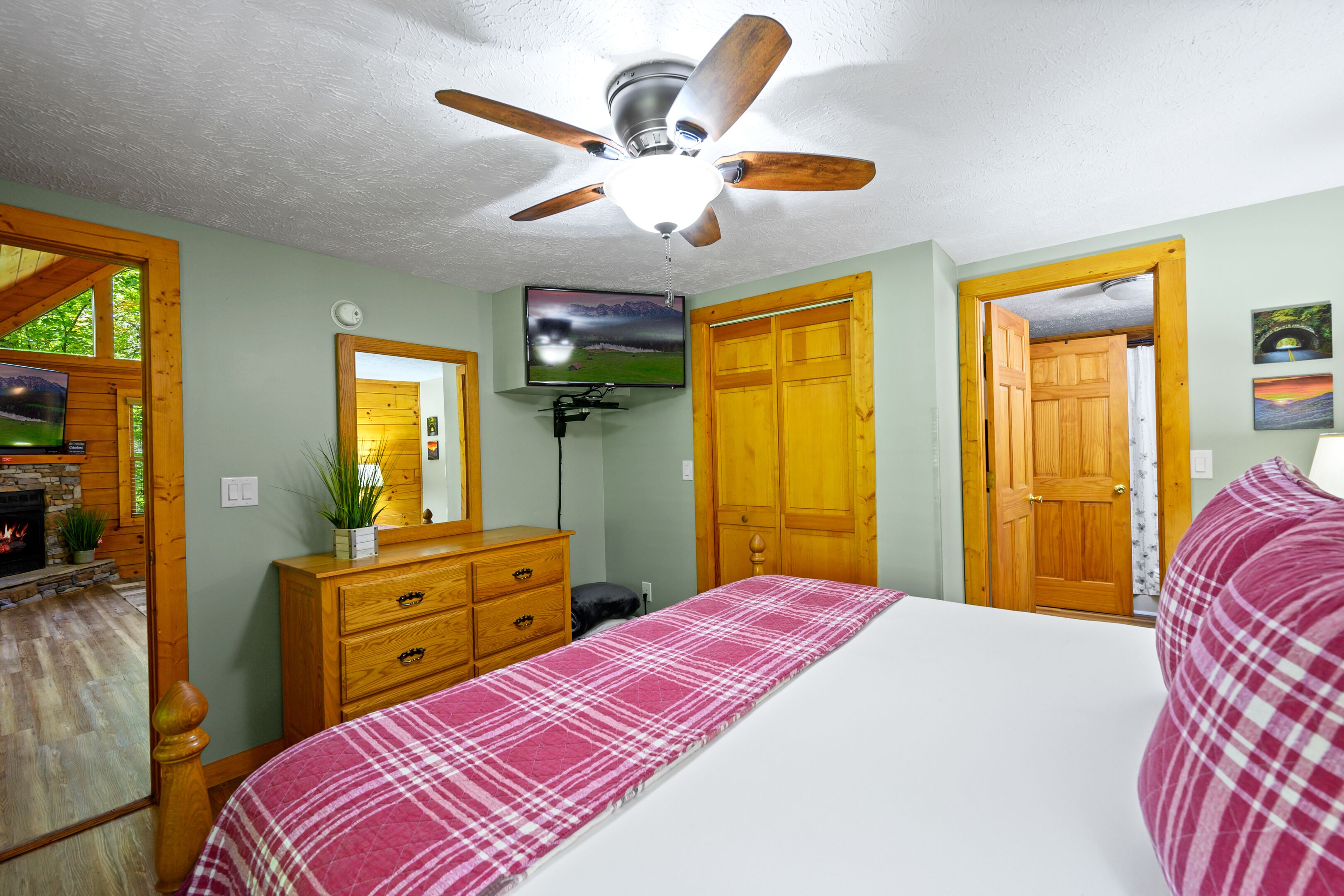 A bedroom with a bed, wooden dresser, ceiling fan, TV, and a fireplace.