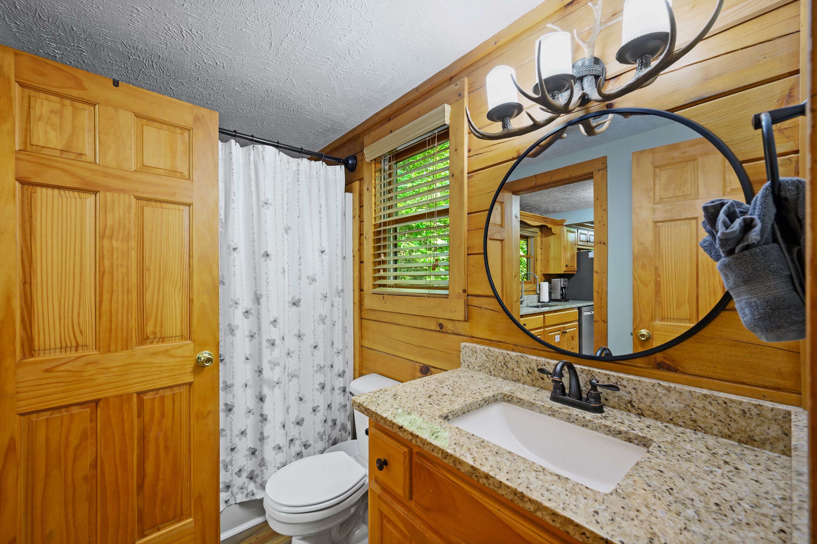 A bathroom with wooden paneling, a white toilet, a granite countertop sink, and a mirror with a towel hanging on it.